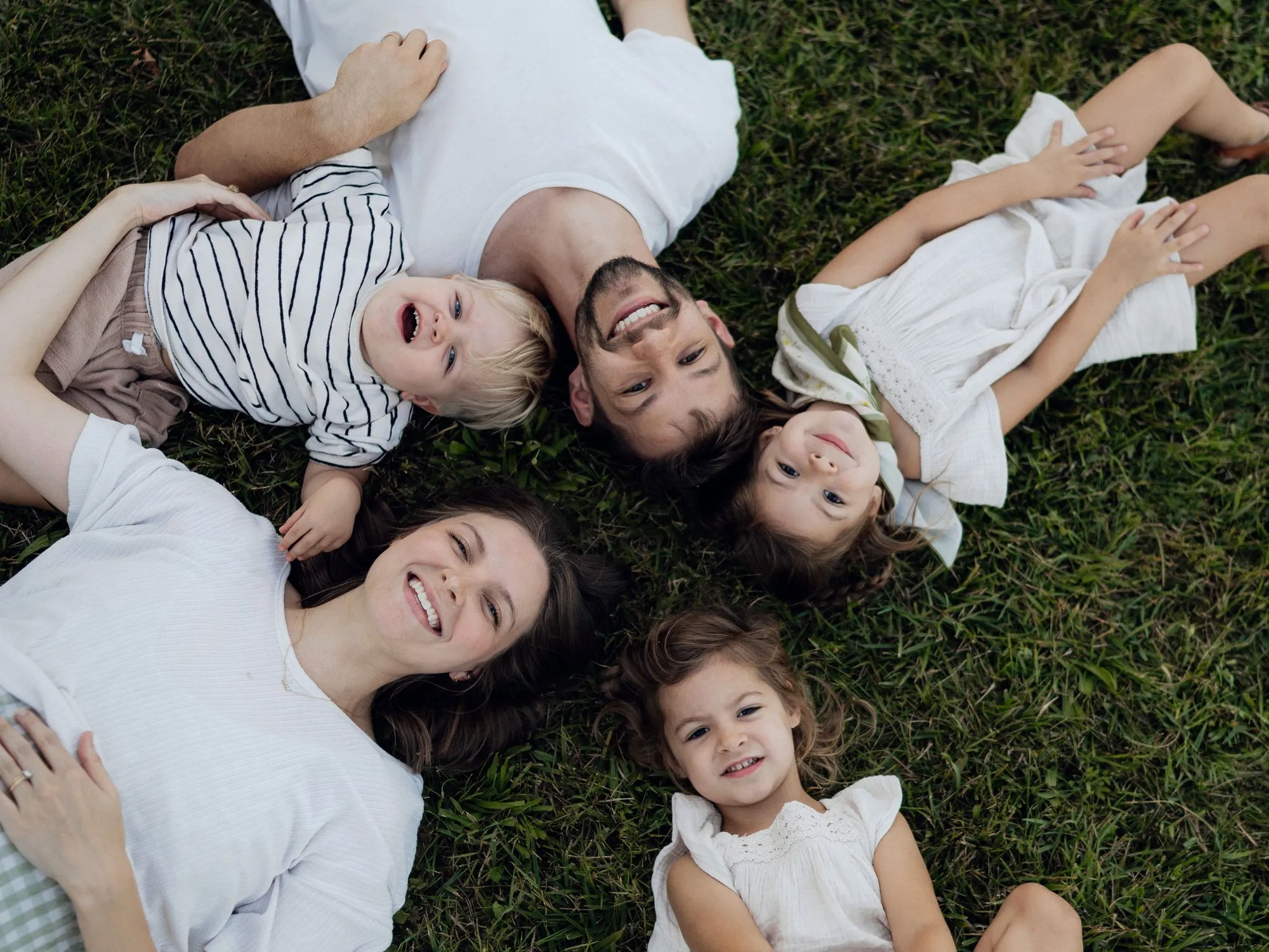 Eine Familie mit drei Kindern liegt im Kreis im Gras, alle lachen in die Kamera.