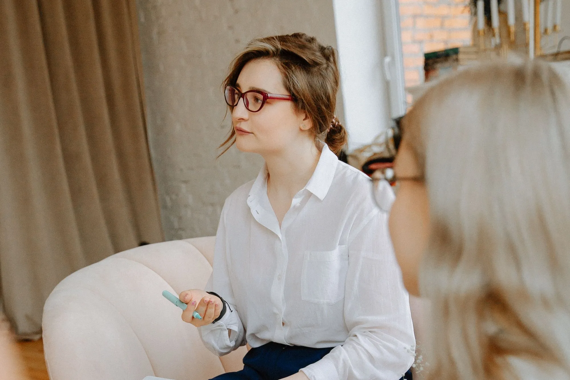 Eine Frau mit Brille sitzt mit einem Notizbuch im Sessel und hört in einer Gesprächsrunde zu.